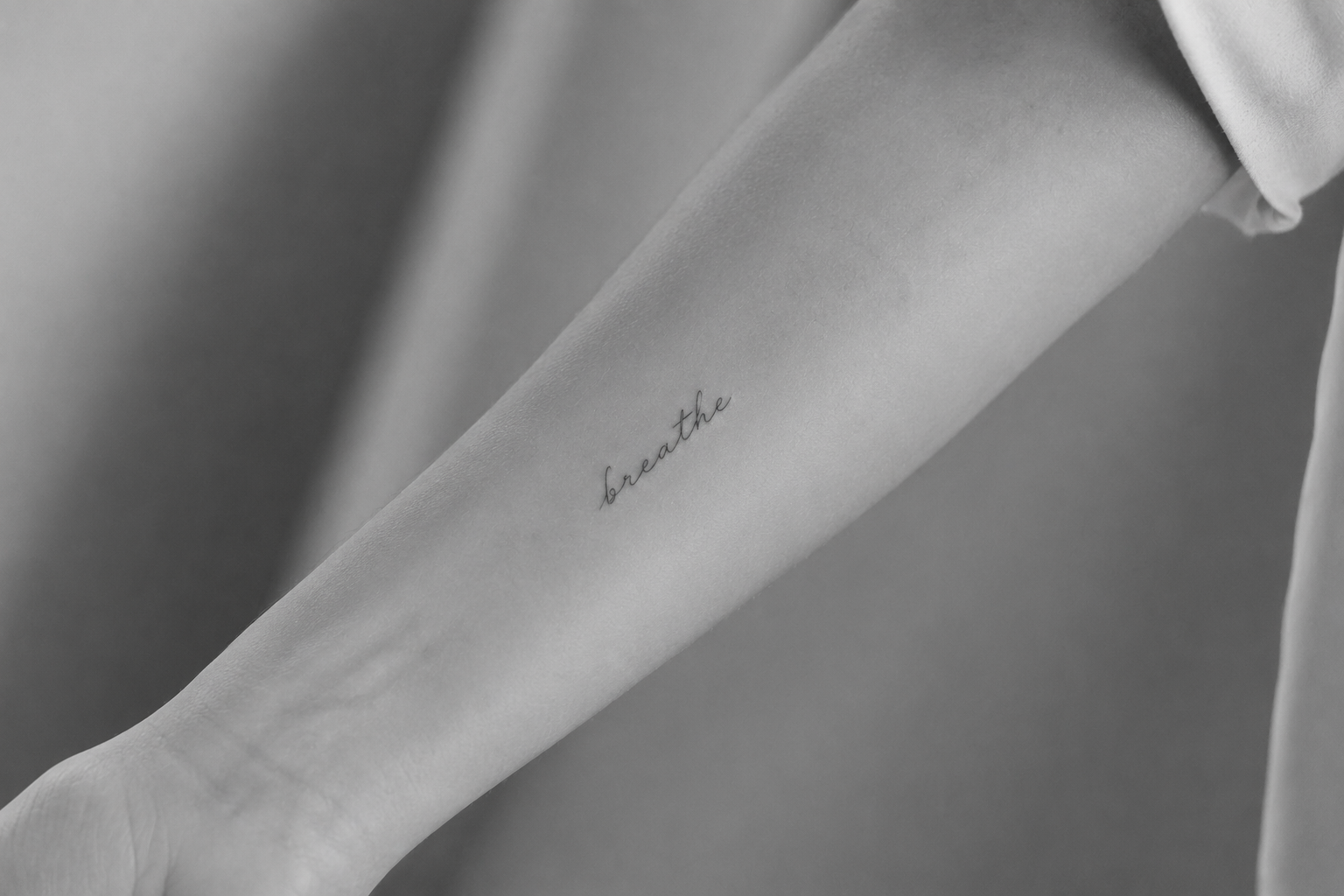 Tatuaje caligráfico 'breathe' en antebrazo